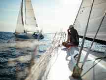 Gothaer Bootsversicherung: Junger Mann sitzt an der Spitze seines Segelboots und schaut über das Wasser